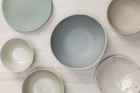 Group of empty blank ceramic round bowls and plates on white stone blackground, Top view of traditional handcrafted kitchenware conceptの写真素材