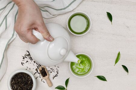Hand pour hot steaming tea into cup from teapot and dried herb tea on the white stone table creative flat lay, Organic product from the nature for healthy with traditional styleの写真素材