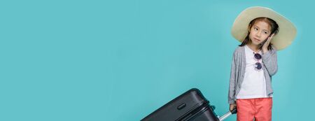 Asian little girl is using a smartphone to check flight to travel on weekends, empty space in studio shot isolated on colorful blue long banner backgroundの写真素材
