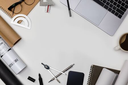 Top view workspace mockup of architectural project with laptop computer, roll blueprints, architectural project plan, engineering tools, office supplies and hot coffee cup on white desk empty spaceの写真素材