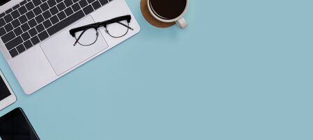 Creative flat lay of office supplies mockup with notebook, hot coffee cup, glasses and accessories isolated on blue long banner background, Top view with copy space, Workspace for freelancerの写真素材