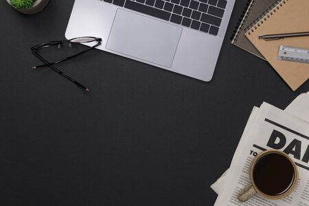 Creative flatlay of office supplies mockup with notebook, hot coffee cup, pen, glasses, books, newspaper and accessories on black desk topview with copy space, Workspace for freelancer backgroundの写真素材