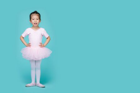 Beautiful smiling Asian little girl in a pink suit is dancing a ballet at school, empty space in studio shot isolated on colorful blue backgroundの写真素材