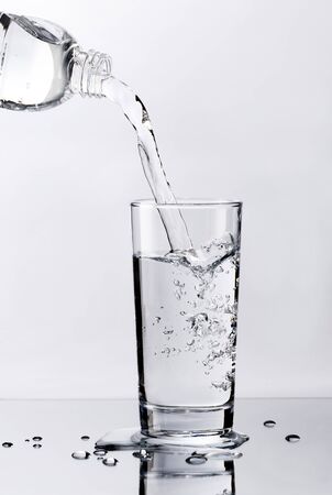 Pouring fresh pure water from bottle into a glass on the table with water drops, Healthcare and beauty hydration conceptの写真素材