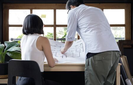 Young man and young woman architecture freelance looking at the blueprint working from home...
