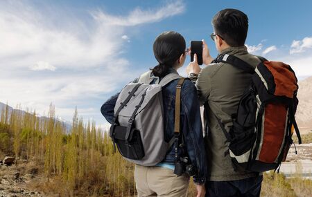 Young traveler man and girl with the backpack on the top of mountain and using smartphone searching...