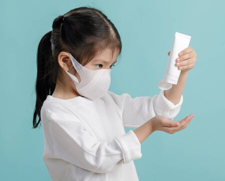 Asian little child girl wearing respirator mask to protect coronavirus outbreak and washing hands with alcohol gel, New virus Covid-19  concept, isolated on blue backgroundの写真素材