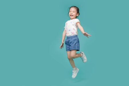 Excited Asian little girl jumping in mid-air, empty space in studio shot isolated on colorful blue backgroundの写真素材