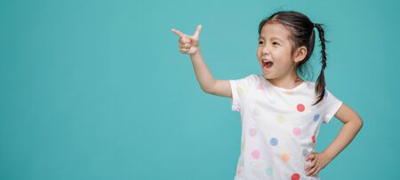 Beautiful smiling Asian little girl pointing hand to blank speech bubble, empty space in studio shot isolated on colorful blue background, Educational concept for schoolの写真素材