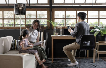 Working from home lifestyle father using smartphone on the desk and child girl learning with her mother on sofa in the living room, Quarantine isolation during the Coronavirus (COVID-19) health crisisの写真素材