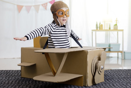 Asian little child girl playing with cardboard toy airplane handicraft in living room with copy space for your text, Creative at home and dreams of flight conceptの写真素材