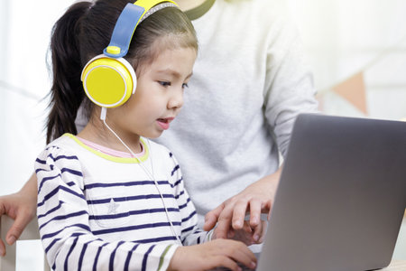 Asian little child girl learning at home with laptop computer using meeting online app with her mother, Quarantine isolation during the Coronavirus (COVID-19) health care, online education conceptの写真素材