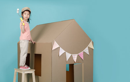 Asian little child girl painting her cardboard house isolated on blue long banner with copy space for your text, Creative at home with family conceptの写真素材