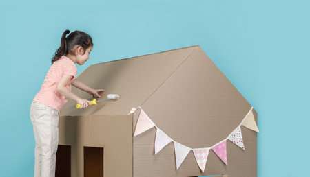Asian little child girl painting her cardboard house isolated on blue long banner, Creative at home with family conceptの写真素材