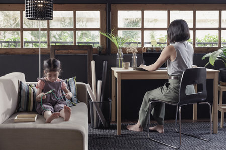 Working from home lifestyle mom using smartphone on the desk and her child girl learning the toy on sofa in the living room, Quarantine isolation during the Coronavirus (COVID-19) health crisisの写真素材