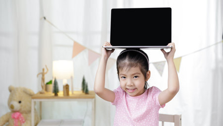 Asian little child girl learning at home with laptop computer using meeting online app, Quarantine isolation during the Coronavirus (COVID-19) health care, online education conceptの写真素材