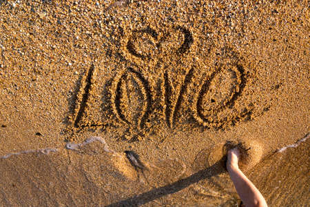 Woman writes with her finger the word love on the sandy seashore.の写真素材