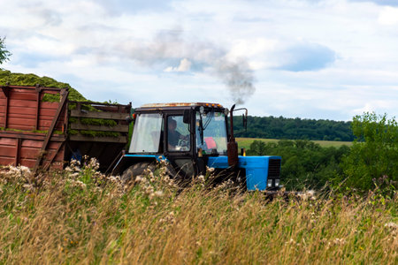A tractor with a trailer drives along the road between fields.