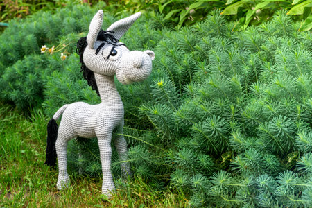 Handmade soft toy amigurumi gray donkey among the greenery of the garden in summer.の写真素材
