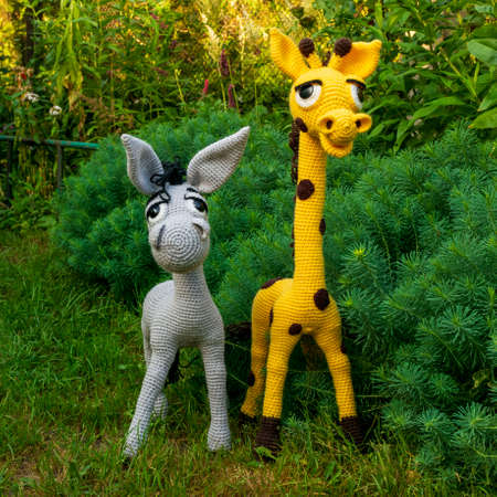 Handmade amigurumi dolls, a yellow giraffe and a gray donkey among the greenery of the garden.の写真素材