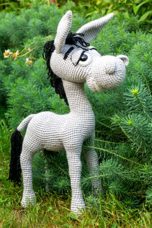 Handmade soft toy amigurumi gray donkey among the greenery of the garden in summer.の写真素材