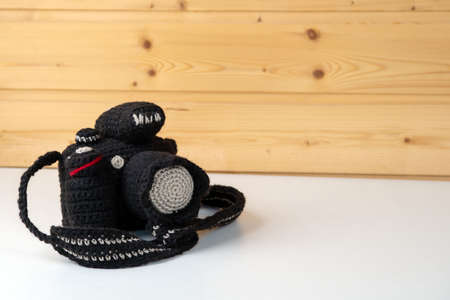 Knitted toy camera mockup with lens and strap on a wooden wall background.の写真素材