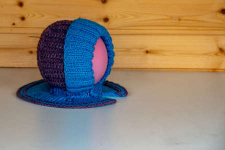 A cute children's knitted hat of a combined color on a background of a plank wall, close-up.