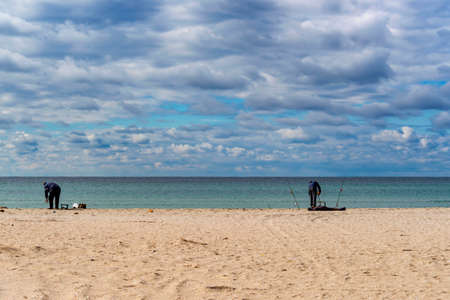 Fishermen catch fish on the sandy shore of the Sea with fishing rods