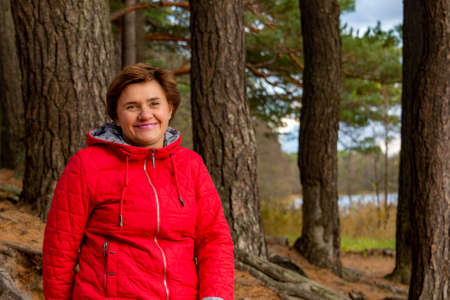 A happy woman in a red jacket smiles in a pine forest on a walk.の写真素材
