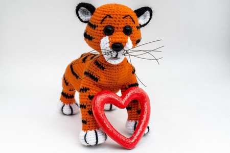 Handmade amigurumi doll tiger cub is standing next to a red heart. The background is white. isolate.の写真素材