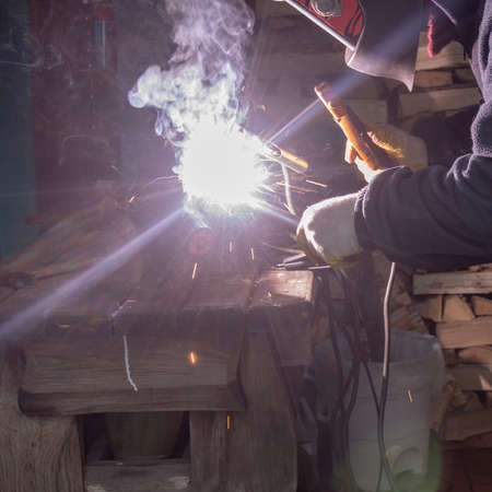 A man in a protective mask welds a metal rod with an electrode.Electric welding of metal products using a converter.の写真素材