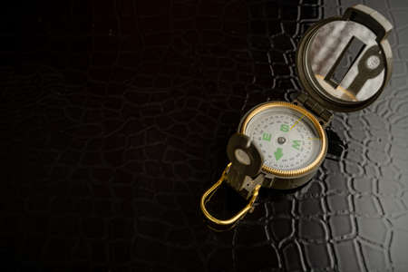 A magnetic compass with a heliograph lies on a black surface. There is free space for text.