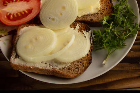 Sandwiches with butter, onions and vegetables lie on plates. Dark wood background.