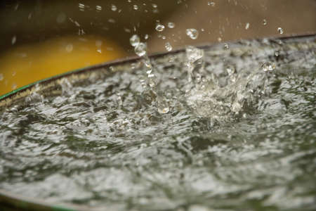 A trickle of rainwater from the roof flows into a full barrel and scatters into small splashes.の写真素材