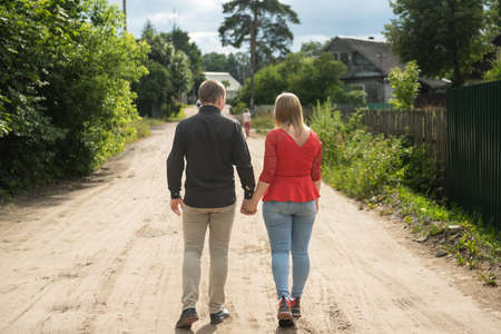 The man and woman hold hands as they walk away along the road.の写真素材