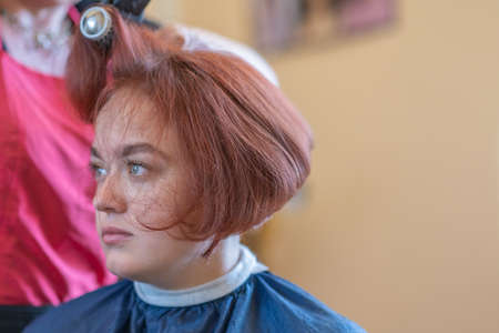 A brown-haired girl is sitting in a chair at the hairdresser doing her hair and styling her hair.の写真素材