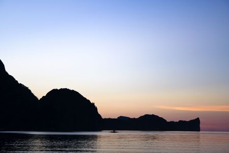 distant outrigger and karst landscpae at sunset el nido palawan island, in the philippinesの写真素材