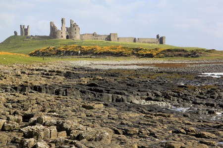 rocky coastline of the northumberland coast of england and the ruins of Dunstanburgh castleの写真素材