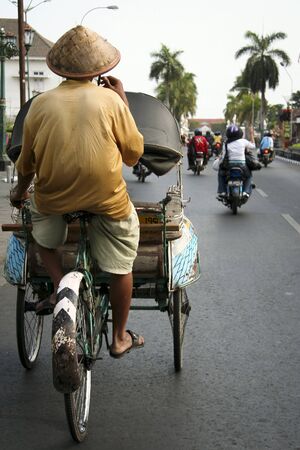 tricycle rickshaw rider being passed by motorcycle traffic on the streets of yogyakarta java indonesiaのeditorial素材