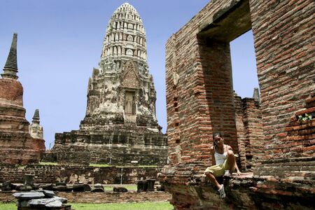 asian woman sitting in frame of collapsed building in the temple ruins of the ancient city of ayuthaya in thailandの写真素材