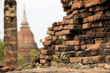 old crumbling overgrown birck wall in front of stupa in the temple ruins of wat mahathat in sukhothai historic park thailandの写真素材