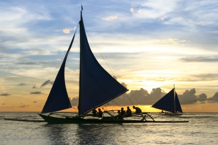 tourists onboard paraw traditional outrigger sailing boats at sunset tours along the coast of boracay island in the philippinesの写真素材