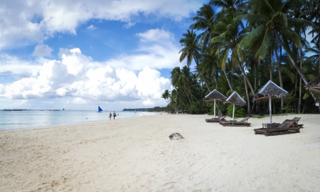 empty sun loungers under tall palm trees lining the white sand beach of boracay island in the philippinesの写真素材