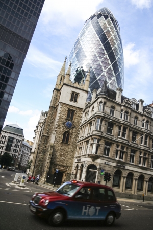 London, England - July 28 2007 : Red colored Taxi cab driving through the city of london past the gherkin skyscaper.のeditorial素材
