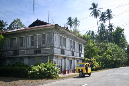 Camuigan Island, Mindanao in the Philippines - May 7 2007: Tricycle Passes Traditional Filipno House - tricycles are customised motorcycles which  provide affordable public transport services to rural communities in the Philippinnesのeditorial素材