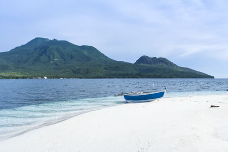 traditional banka outrigger canoe on white beach cauin island, mindanao in the philippines, with volcano in the backgroundの写真素材