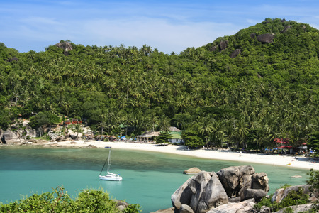 white sailboat anchred in beautiful crystal bay surrounded by jugle clad hills near lamai on ko samui island in the gulf of thailandの写真素材