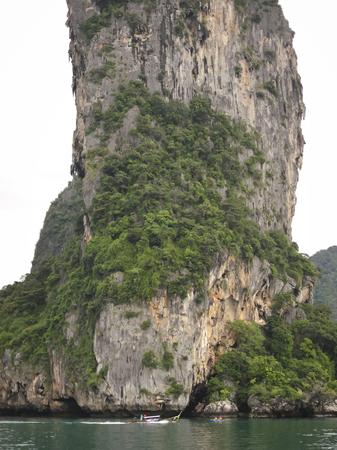traditional thai longtail boat passing tourists in kayak with dramatic limestone cliffs of krabi coastline behindの写真素材