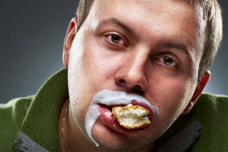 Closeup portrait of funny man. Yogurt traces on his lips, mouth full of breadの写真素材