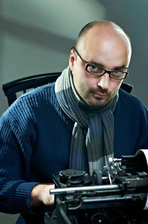 Old fashioned bald writer in glasses writing book on a vintage typewriterの写真素材